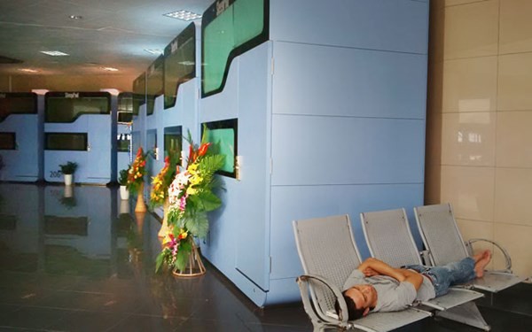 Một hành khách nằm ngủ trên hàng ghế cạnh hộp ngủ ở sân bay Nội Bài.